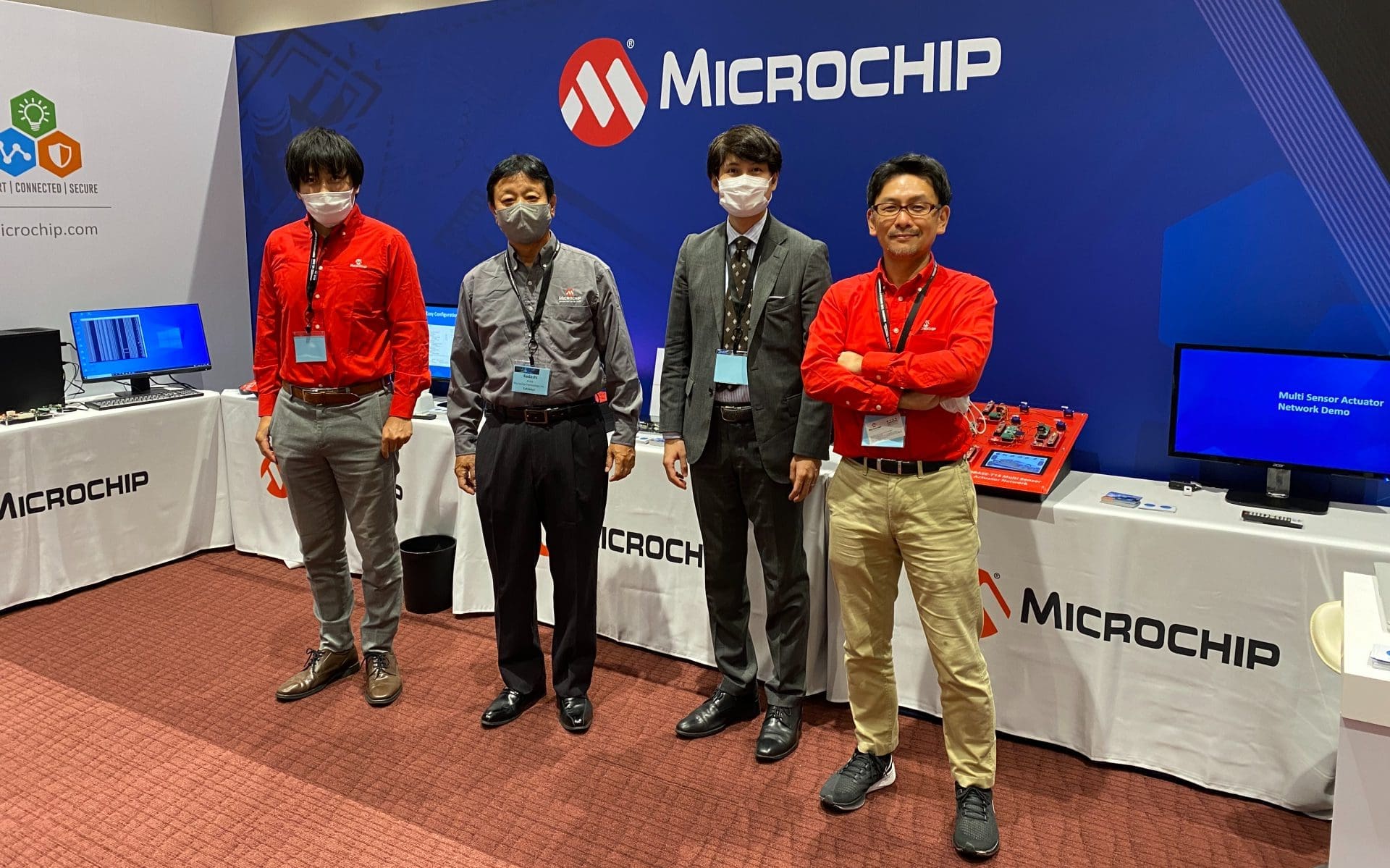 Four men with lanyards stand before an event table with the logo 