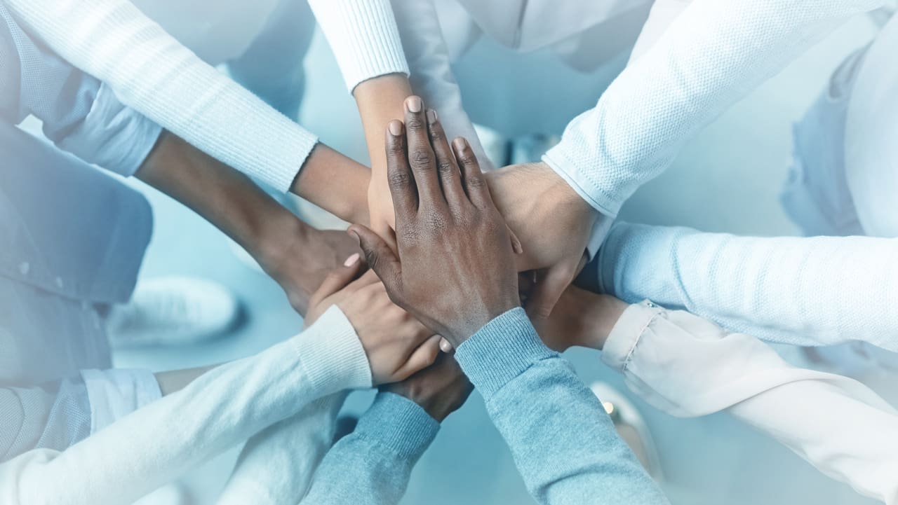 Several people putting their hands together in a circle, in the spirit of collaboration.