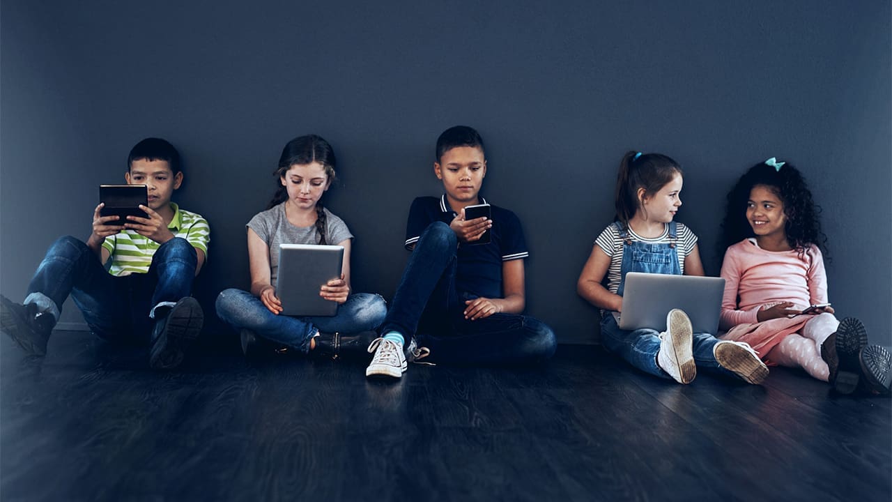 Multiple children sitting on the floor using electronic devices.